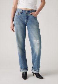 Lichtblauwe denim jeans met een relaxte pasvorm, voorzien van versleten accenten en opgerolde cuffs, gecombineerd met zwarte hoge hakken.
