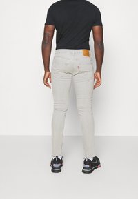 Ljusgrå skinny jeans med en lätt stretch, med en brun läderlapp bak, bakfickor och en mjuk textur. Svarta sneakers nedanför.