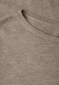 Vaaleanbeige neulepaita, jossa on ribattu pyöreä pääntie ja sileä pinta. Sisältää hienovaraisen kuosin ja päällekkäisen kankaan kaula-aukossa.