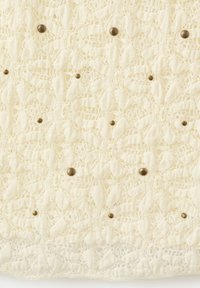 Tissu en dentelle crème avec motif floral, orné de petits clous ronds en bronze répartis uniformément sur la surface.