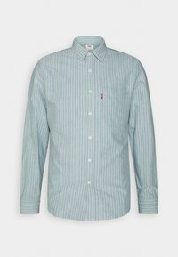 Chemise à manches longues boutonnée avec des rayures verticales bleu clair et blanc et une poche poitrine avant avec une étiquette rouge.