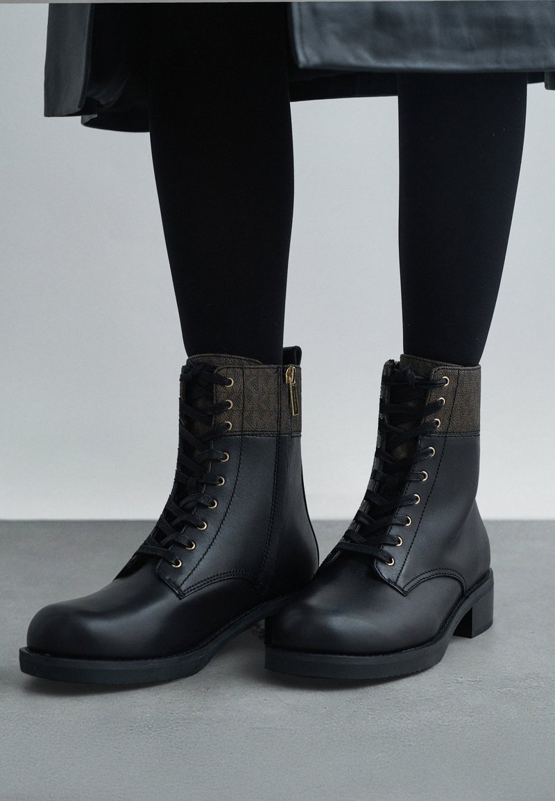 Bottines noires avec un col texturé marron, des œillets dorés et des zips sur les côtés. Tige en cuir lisse et semelle en caoutchouc.