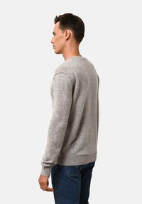Grauer Pullover mit langen Ärmeln, Rundhalsausschnitt und gerippten Bündchen und Saum. Über blauen Jeans getragen, zeigt er eine weiche Textur und ein lässiges Design.