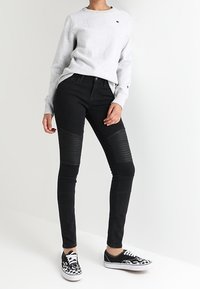 Černé skinny džíny s jemnou texturou na stehnech. Komplet s světle šedou mikinou a černo-bílými teniskami s potiskem.