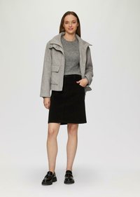Graue Wollmischjacke mit hohem Kragen, Fronttaschen und einem schwarzen Denim-Rock. Das Modell trägt schwarze Loafer mit dicker Sohle.