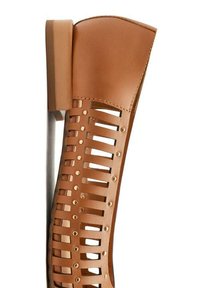 Stivaletto in pelle tan con design a strisce ritagliate, caratterizzato da dettagli circolari dorati.Parte superiore liscia, tacco rettangolare.