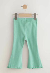 Menta zöld bordázott, bővülő nadrágok, fa vállfán bemutatva, alul hullámos szegélydíszítéssel és sima felülettel.