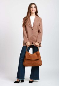 Blazer in tessuto marrone con due bottoni, abbinato a jeans scuri a zampa e una grande borsa in camoscio marrone con manico a catena. Décolleté nere.