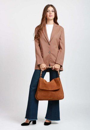 Blazer in tessuto marrone con due bottoni, abbinato a jeans scuri a zampa e una grande borsa in camoscio marrone con manico a catena. Décolleté nere.