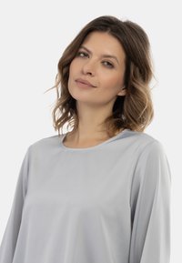 Világosszürke, hosszú ujjú felső, kerek nyakkivágással. Simás textúra és laza szabás. Folyó ujjak és diszkrét varrási részletek jellemzik.