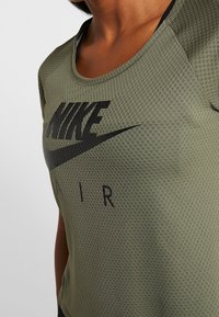 Camiseta Nike verde oliva con un diseño de malla texturizada; cuenta con un cuello redondo y un prominente texto de logotipo negro "NIKE AIR" en el frente.