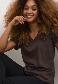 T-shirt marrone a V in morbido tessuto, con maniche corte e vestibilità comoda, abbinato a pantaloni neri.