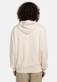 Sudadera beige hecha de material suave, con capucha, hombros caídos y puños y dobladillo de canalé. El diseño es relajado y de corte oversize.