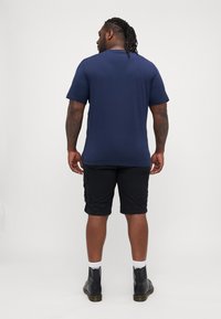 T-shirt blu navy a maniche corte realizzato in tessuto liscio, abbinato a pantaloni cargo neri. Stivali alla caviglia neri e calzini bianchi completano l'outfit.