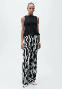 Haut peplum noir associé à un pantalon à jambes larges rayé zèbre en blanc et noir. Accentué par un bracelet simple et des talons ouverts.