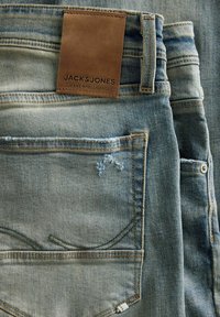 Pahuljica svijetloplavih traperica s vidljivim stražnjim džepom, petljom za pojas i smešnom kožnom oznakom marke "Jack & Jones."