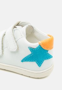 Fehér bőr sneaker kék velúr csillag díszítéssel és narancssárga sarkú betéttel. Különleges jellemzője a tépőzáras pánt és a texturált gumitalp.