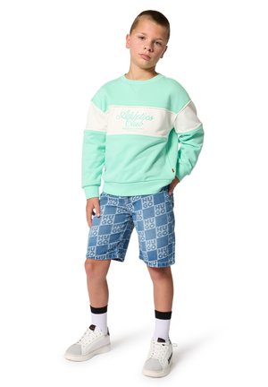 Garçon debout, main dans la poche, portant un sweat-shirt vert menthe et blanc avec l'inscription « Athletics Club » et un short bleu à motifs avec l'impression « HUGO ».