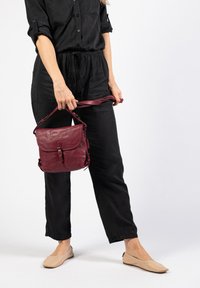 Bordeaux leren crossbody tas met een klep sluiting, verstelbare schouderriem en zijhardwaredetails. Gladde textuur en compacte vorm.
