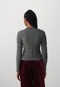 Graues Langarmshirt mit strukturiertem Blumenmuster, Rundhalsausschnitt und taillierter Form, kombiniert mit bordeauxfarbigen weit geschnittenen Hosen.