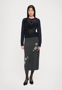 Suéter de malha leve azul-marinho com bordado floral preto, combinado com uma saia lápis cinza com flores bordadas e uma fenda lateral.