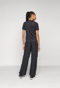 Zwart sporttop met korte mouwen en losse zwarte broek. De stof lijkt lichtgewicht en heeft een zachte textuur. Sneakers zijn zwart met witte zolen.