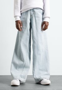 Jeans azzurri a gamba larga realizzati in denim, con vestibilità ampia e vita bassa, abbinati a sneakers bianche per un look casual.