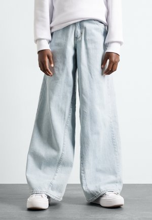 Jeans azzurri a gamba larga realizzati in denim, con vestibilità ampia e vita bassa, abbinati a sneakers bianche per un look casual.