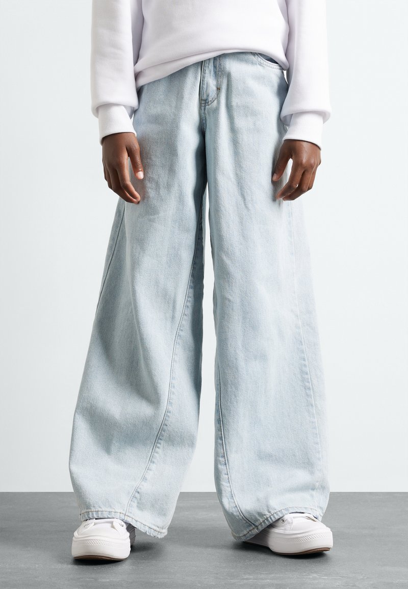Jeans azzurri a gamba larga realizzati in denim, con vestibilità ampia e vita bassa, abbinati a sneakers bianche per un look casual.