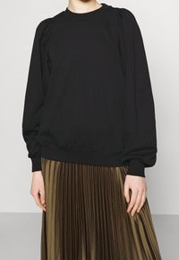 Felpa nera con maniche a sbuffo, colletto e polsini a costine, abbinata a una gonna plissettata verde oliva, design semplice e moderno.