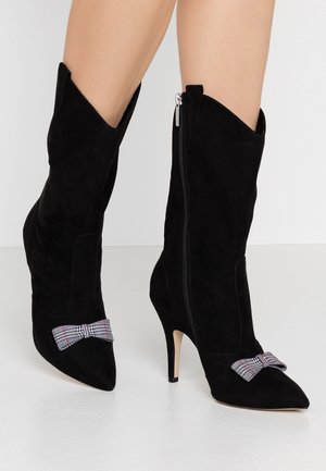 Bottines en suede noir avec des pointes et des talons hauts. Elles présentent une fermeture éclair sur le côté et un accent nœud tartan sur le devant.