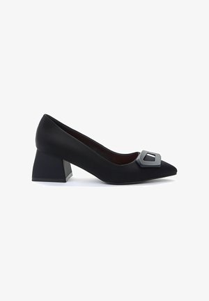 Zwarte stoffen pump met een spitse neus, voorzien van een geometrische gesp aan de voorkant en een chunky, vierkante hak. Gladde textuur.