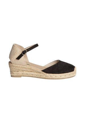 Espadrille de cuña de ante negro con un tacón trenzado de color marrón claro. Presenta una correa de tobillo negra con un hebilla circular y una plantilla beige suave.