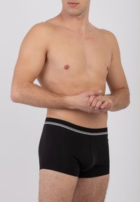 Boxer in cotone nero con design aderente, caratterizzati da una morbida vita decorata con una linea grigia. Il modello è posato di lato.