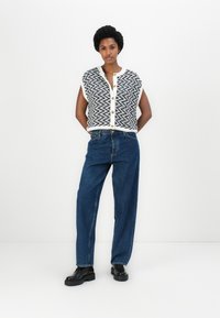 Pletený krátký rukáv top v černo-bílém vzoru cikcaku, s button-up předním zapínáním, spárovaný s vysokým modrým džínami a černými botami.
