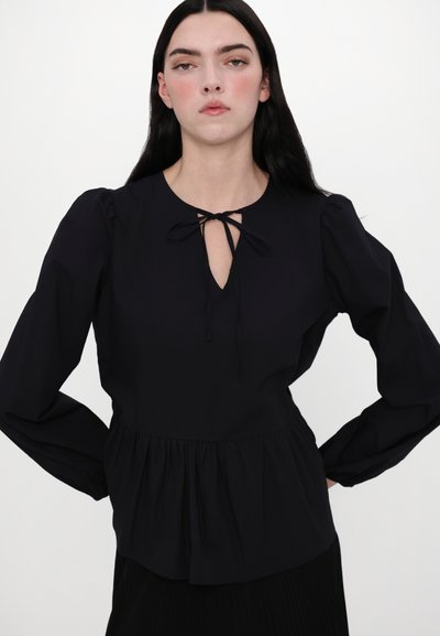 Must // Peplum pluus musta värvi, ümmarguse kaeluse, võtmekuju avause ja nööriga detailiga. Pikad varrukad koos kogutud mansettidega, valmistatud siledast kangast.