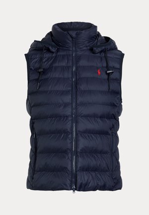 Ung kvinde iført grå joggingbukser, grå sweatshirt, marineblå vatteret vest, mønstret tørklæde og hvide sneakers med off-white sokker.
