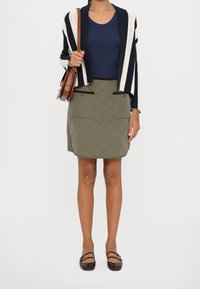 Námořnicky modrý a smetanový pruhovaný kardigan přes námořnicky modrý top, doplněný prošívanou olivovou sukní s hnědým lemováním a hnědými balerínami.