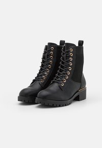 Botas negras hasta el tobillo con un upper de cuero suave, ojales dorados, paneles elásticos laterales, un tacón cuadrado y una suela texturizada.