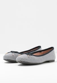 Ballerinas mit einem schwarz-weißen gestreiften Stoffbezug, runder Spitze, schwarzem Rand und dekorativem Schleifenakzent auf der Vorderseite.