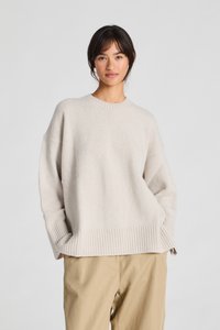 Licht beige gebreide trui met een ribbelzoom, losse pasvorm, verlaagde schouders en een ronde halslijn. Gecombineerd met tan kleurige broek.