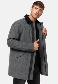 Abrigo de mezcla de lana gris con collar de piel negra, cierre frontal de cremallera y a presión, bolsillos laterales y tejido texturizado. Diseñado para el calor y la comodidad.