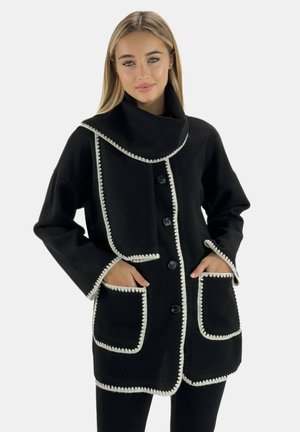 Black coat with oversized collar, button front, and white trim. Features two pockets with contrasting edging. Textured fabric.