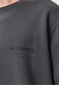 Grå sweatshirt med rund halsudskæring, struktureret stof og trykt logo "ALLSAINTS" med signaturdetalje på fronten.