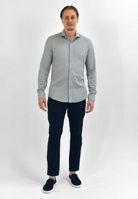 Lichtgrijze lange mouw knoopshirt met een puntige kraag, gecombineerd met marineblauwe slim-fit broeken en zwarte instapschoenen. Glad stoftextuur.