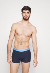 Boxers en coton bleu marine avec une ceinture "TOMMY HILFIGER" bleu clair, offrant une coupe ajustée et des coutures minimales pour plus de confort.