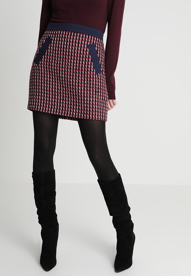 Neulottu minihame, jossa on punavalkoinen ja laivastonsininen ruutukuosi, laivastonsininen vyötärönauha ja kaksi laivastonsinistä taskua. Yhdistetty mustien polven korkeiden saappaiden kanssa.