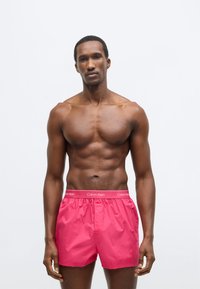 Ροζ μαγιό Calvin Klein με ελαστική μέση και λεπτομέρεια λογότυπου. Λείο ύφασμα, άνετη εφαρμογή, μήκος μέχρι το γόνατο.