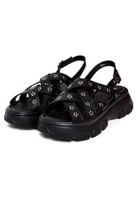 Zwarte plateau-sandalen met kruisspierontwerp, voorzien van zilveren sterstuds en een textuur op de zolen voor grip. Verstelbare enkelriem voor een goede pasvorm.