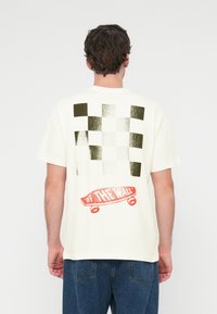 Εκρού T-shirt με μοτίβο σκακιέρας σε πράσινο και άσπρο, με κόκκινο γραφικό skateboard που γράφει «OFF THE WALL» στο πίσω μέρος.